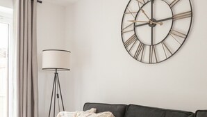 En moderne stue med en grå sofa, et stort vægur og en gulvlampe.