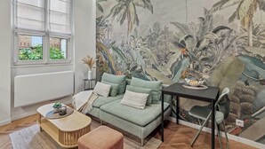 Una sala de estar con un sofá verde, una mesita de madera y un mural con follaje tropical.