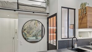 Una cocina moderna con encimera negra, espejo redondo, lavamanos y una cama litera en la parte superior.