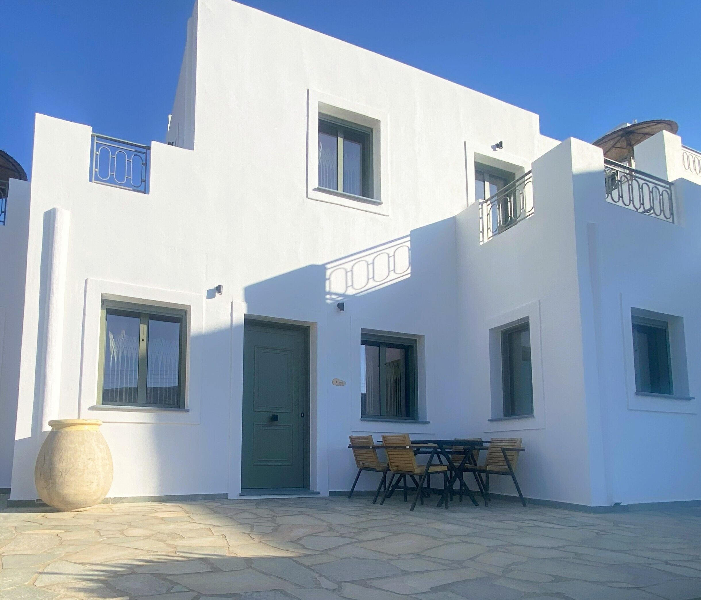 A white building with a green door, a balcony, and a table with chairs in front.
