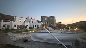 A boat in a courtyard with stone pathways and white buildings. - Ammos Andros Accommodation (Ormos Korthiou)