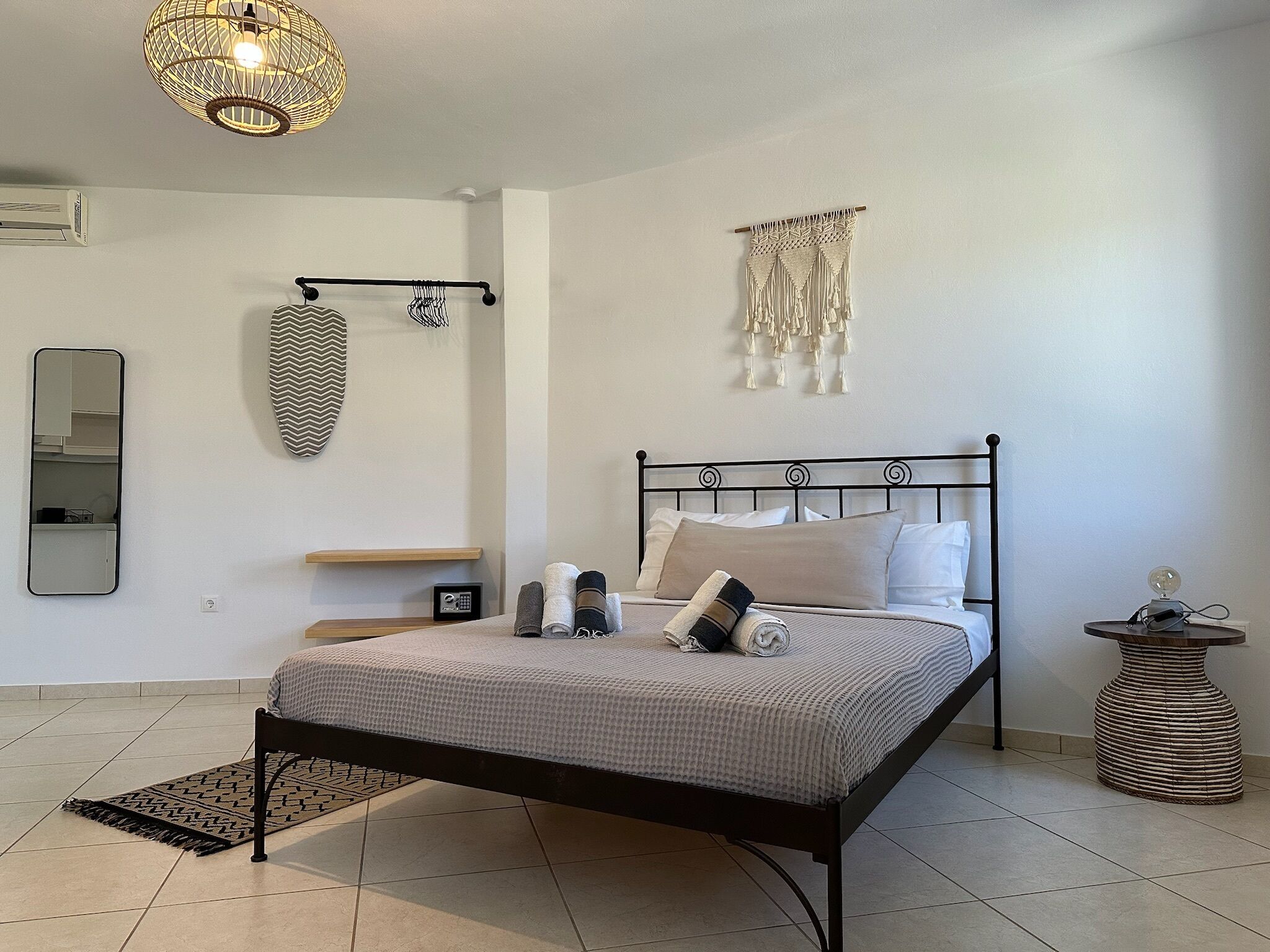 A neatly arranged bedroom with a bed, bedside tables, a hanging macrame decoration, a mirror, and a ceiling light fixture.