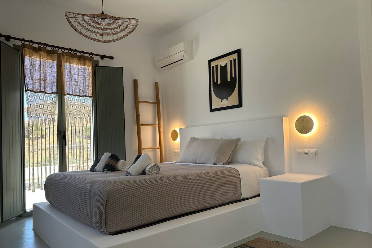 A modern bedroom with a large bed, a ladder, and a wall-mounted air conditioner.