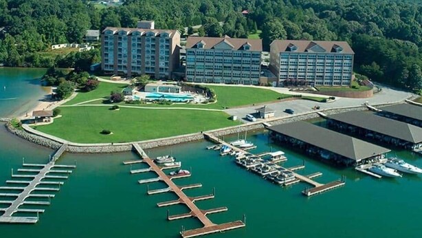 Een groot hotel met meerdere gebouwen, een jachthaven met boten en een bebost achtergrond.