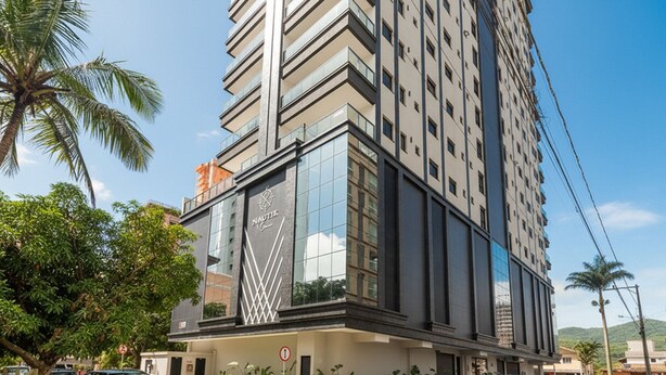 Un grand immeuble moderne à la façade en verre, avec un logo bien visible et un espace de stationnement où sont garées des voitures.