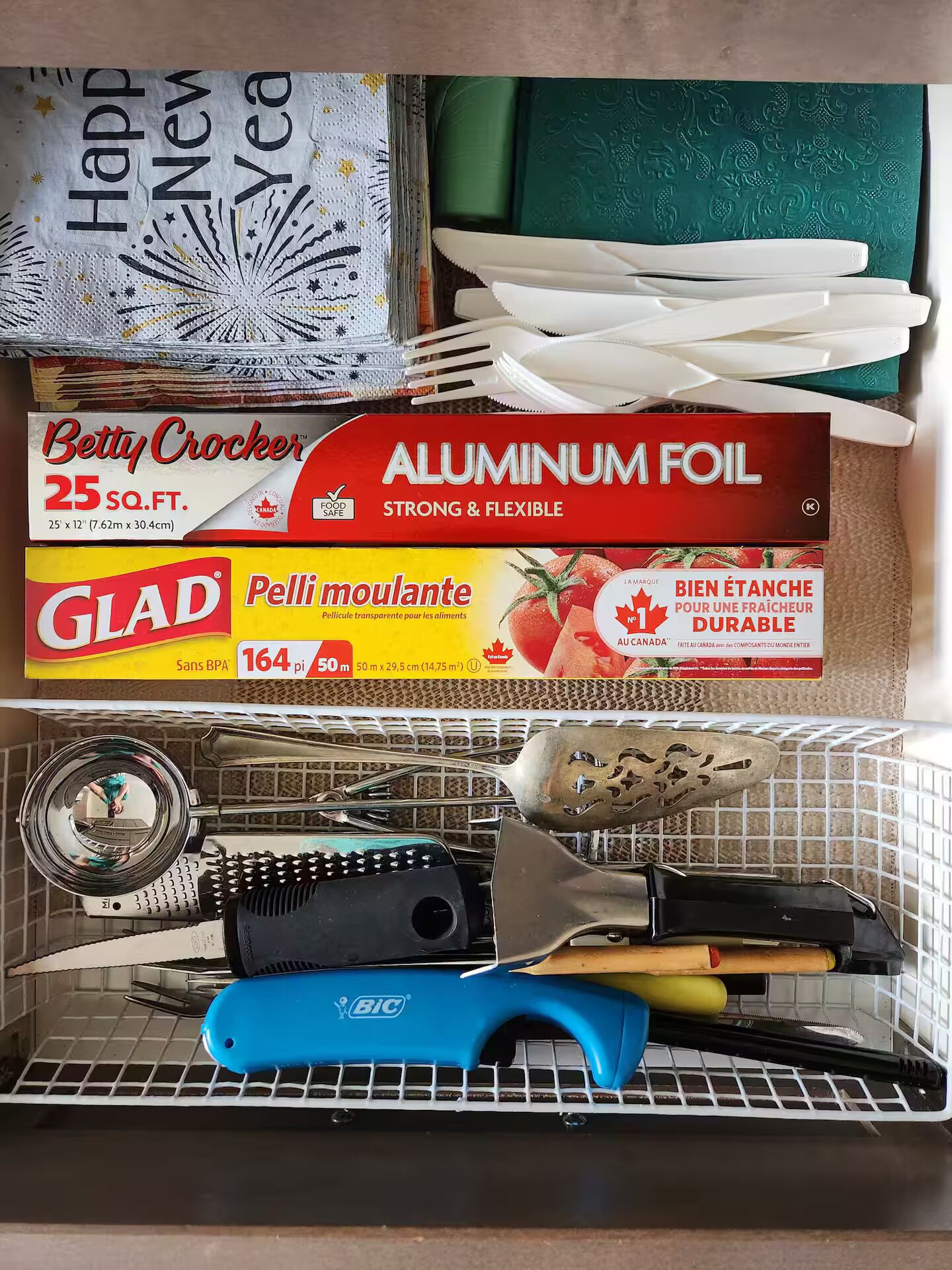 Une cuisine équipée d’une variété d’ustensiles et de casseroles, notamment une boîte de papier d’aluminium Betty Crocker, un film plastique Glad et un ouvre-boîte BIC.
