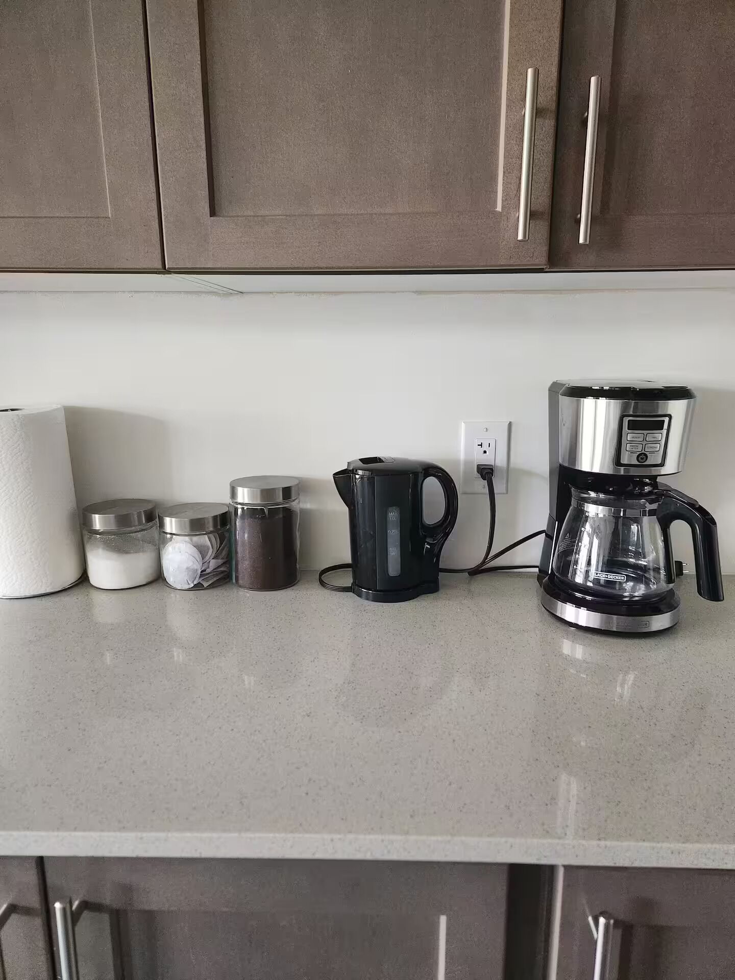 A kitchen counter with a coffee maker, a kettle, and containers of sugar and creamer.