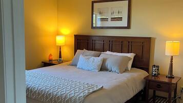 A neatly made bed with a white comforter and pillows, two bedside lamps, a framed picture on the wall, and a wooden nightstand with a lamp.