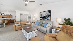 A spacious living room with a beige sofa, a coffee table, and a painting on the wall. - Pet-Perfect Village Retreat with Fenced Yard in a Prime Spot – Book & Save (The Villages)