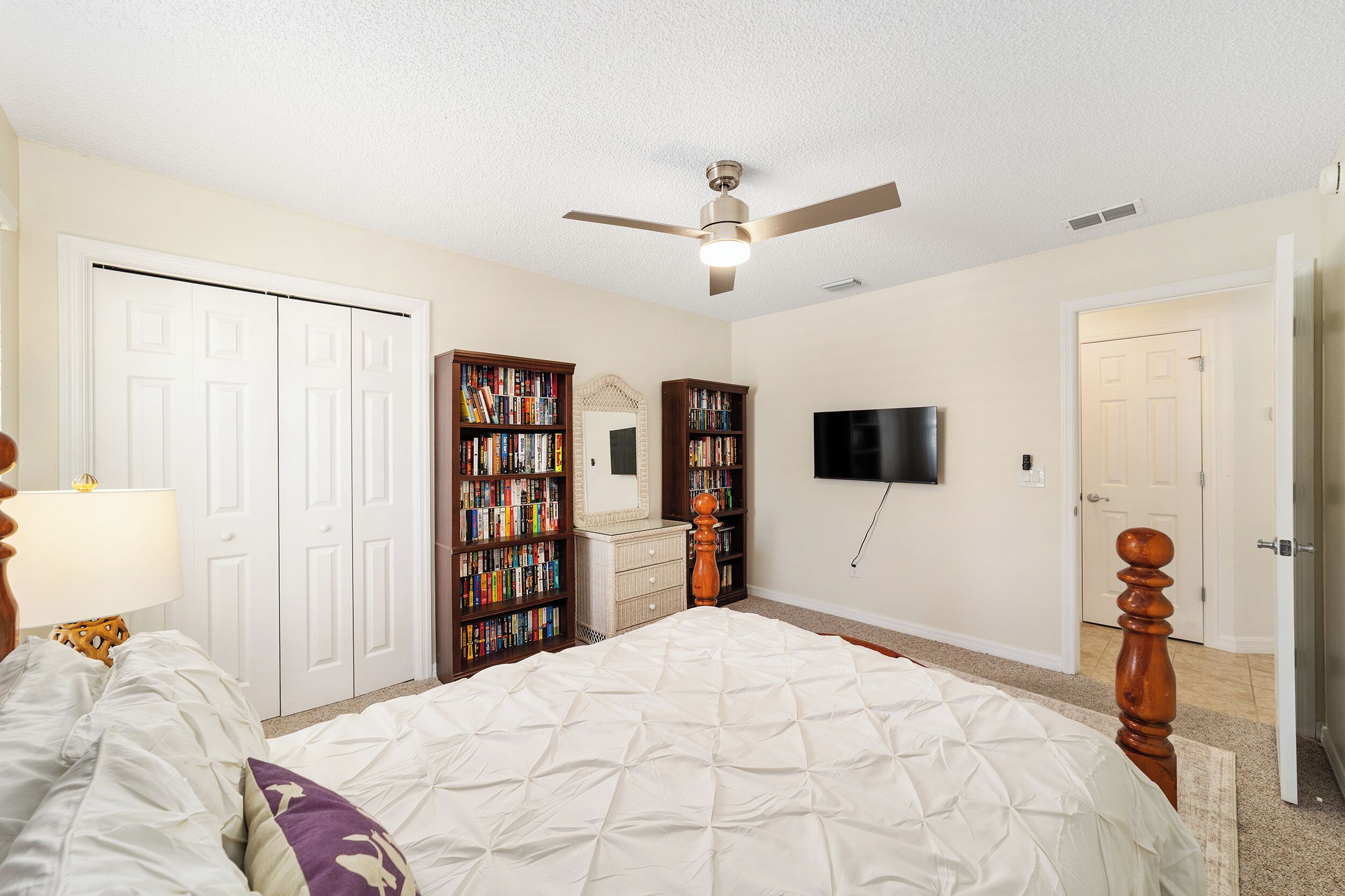 Ein Schlafzimmer mit Bett, Deckenventilator, Fernseher und Bücherregalen.
