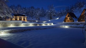 Lumipeitteinen maisema, jossa kivestä rakennettu polku johtaa puiseen mökkiin.