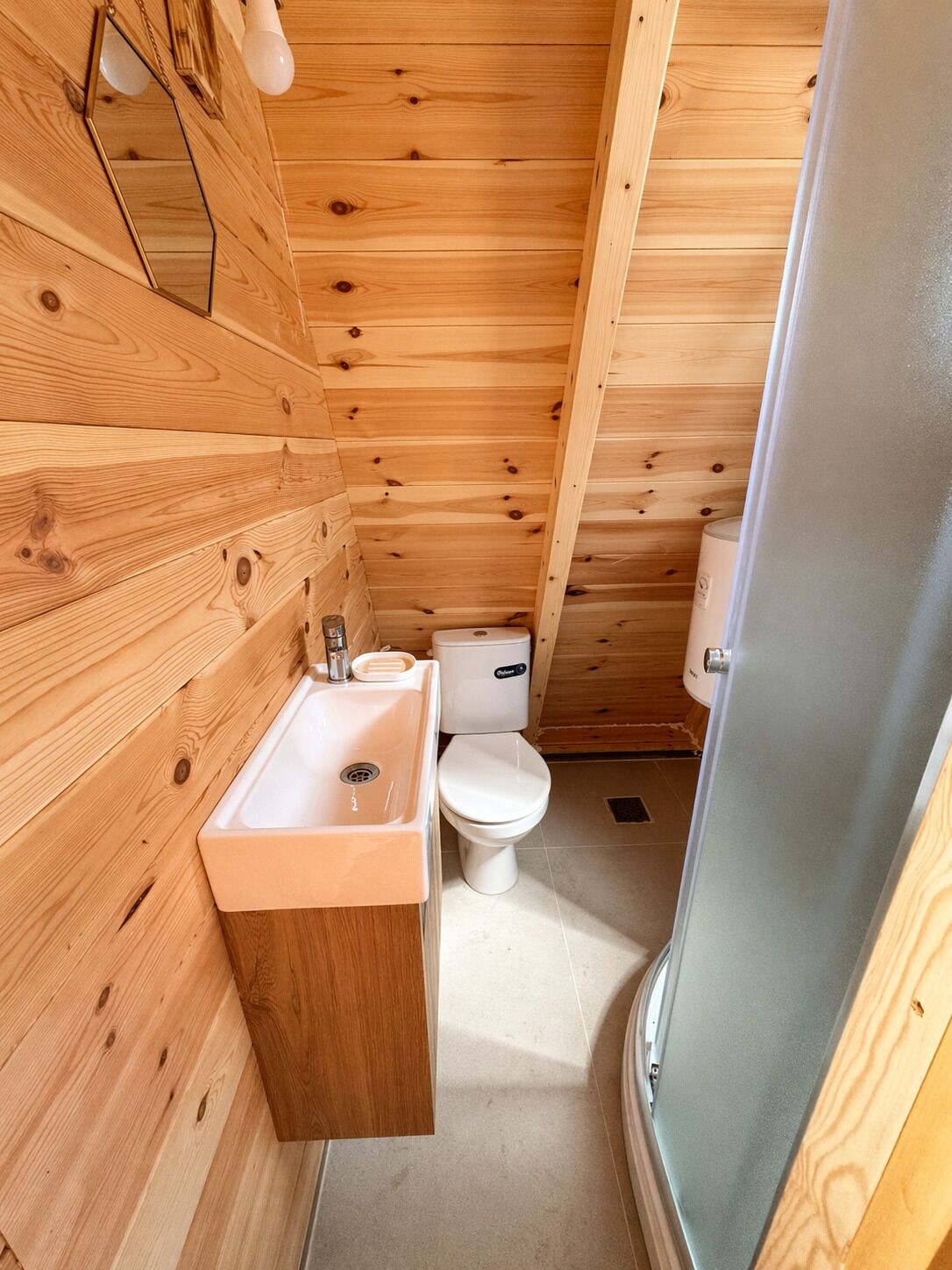 Baño de una cabaña de madera compacta, con lavamanos, inodoro y zona de ducha.