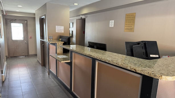 Un espace d’accueil d’hôtel avec un comptoir en marbre, un extincteur et un panneau indiquant les heures d’arrivée et de départ ainsi que les services proposés.