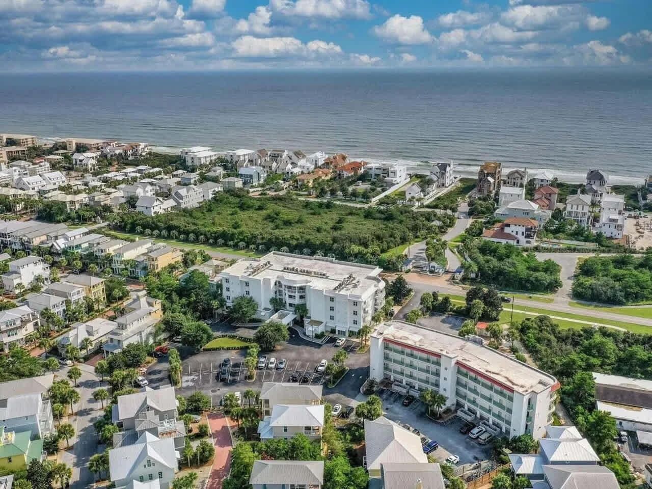 An aerial view of a coastal town with a prominent hotel featuring a central courtyard and multiple parking areas.