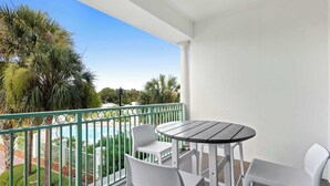 A balcony with a table and chairs, overlooking a pool and greenery. - The Inn at Seacrest Beach Unit 207 (Alys Beach)