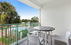 A balcony with a table and chairs, overlooking a pool and greenery. - The Inn at Seacrest Beach Unit 207 (Alys Beach)
