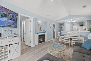 A spacious living room with a fireplace, a dining area, and a kitchen. - Surf & Sail | cozy with TONS of amenities (Myrtle Beach)