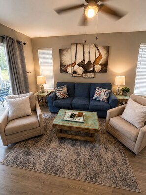 A living room with a blue sofa, two armchairs, a coffee table, and a ceiling fan. - 19th Hole in Waterway Village (Myrtle Beach)