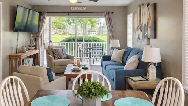 Un salon comprenant un canapé, des fauteuils, une table à manger, un téléviseur et un balcon avec vue.