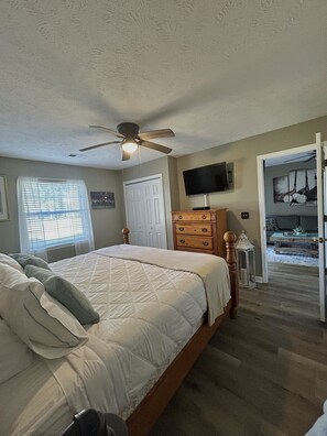 A bedroom with a bed, a ceiling fan, a dresser, a television, and a door leading to another room. - 19th Hole in Waterway Village (Myrtle Beach)