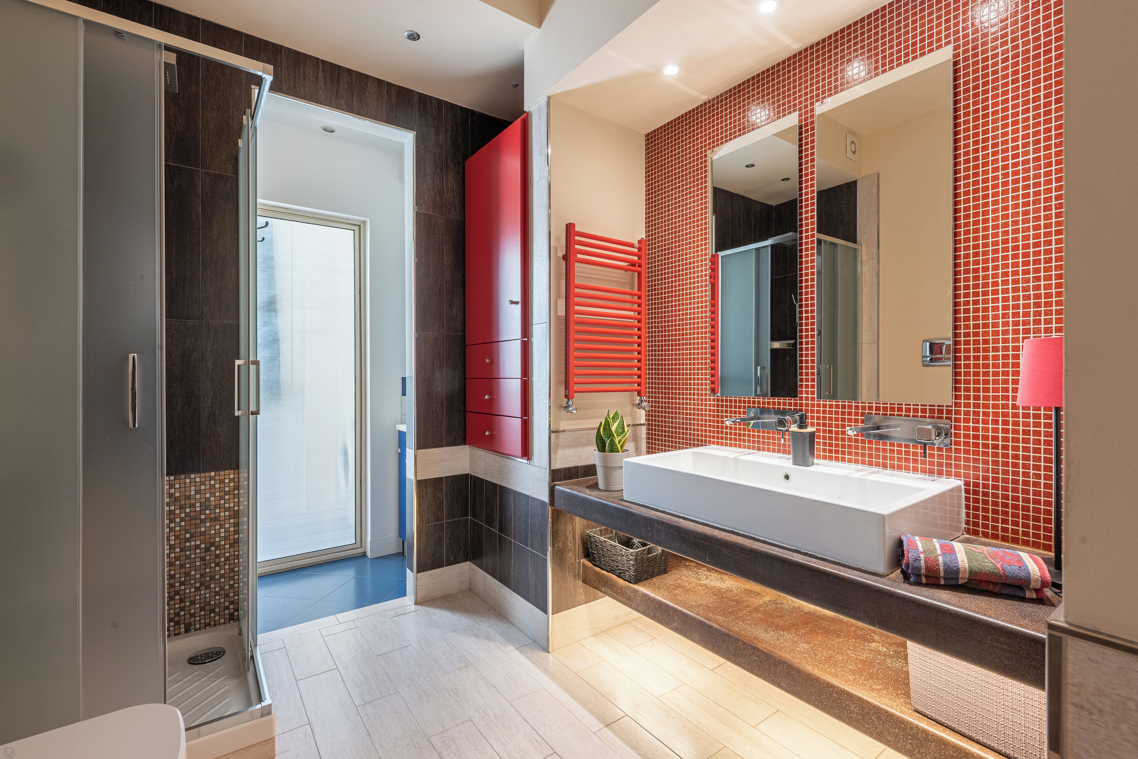 A modern bathroom with a large mirror, a red cabinet, and a shower area.