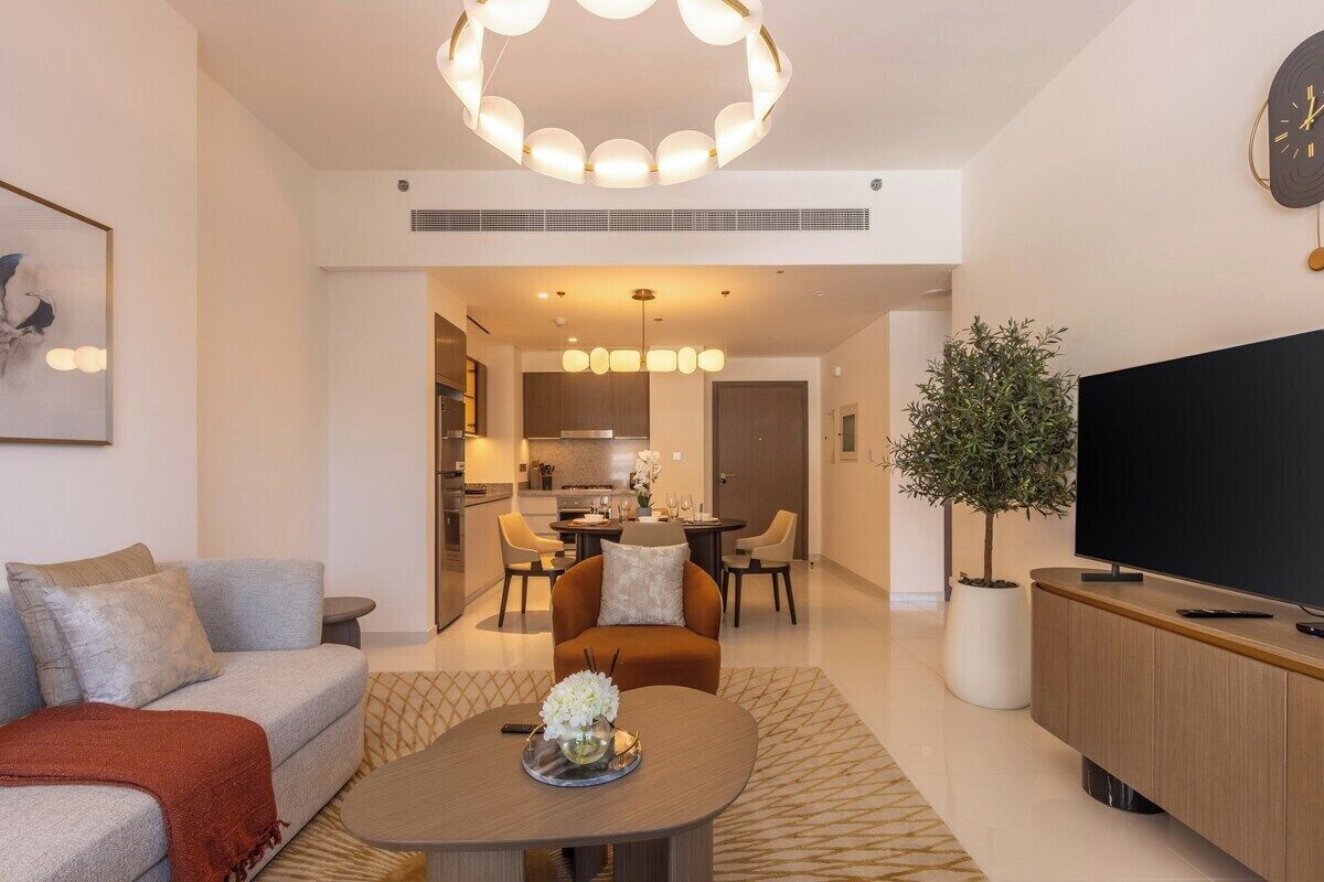 Un salon moderne avec un canapé, une table basse et un meuble pour la télévision. On y trouve également un coin repas avec des chaises et une table, ainsi qu’une cuisine en arrière-plan.