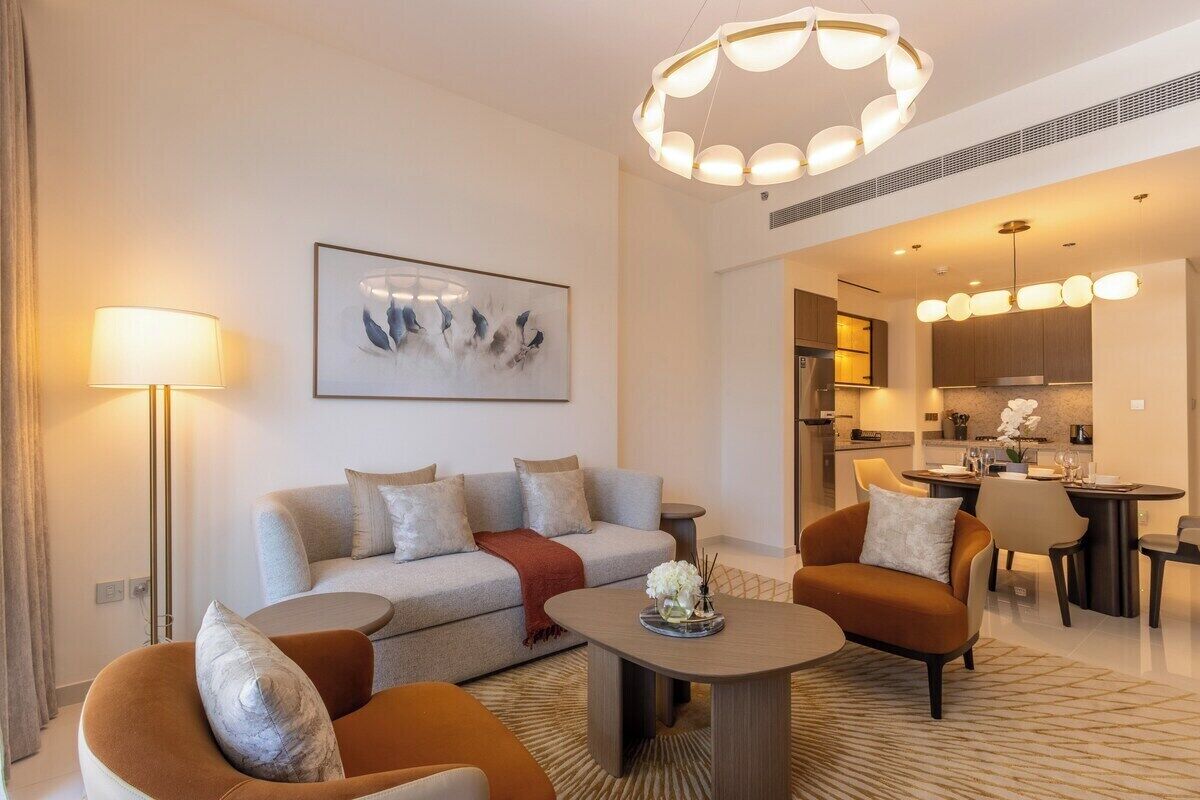 Een moderne woonkamer met een bank, fauteuils, een salontafel en een eethoek met een kroonluchter.
