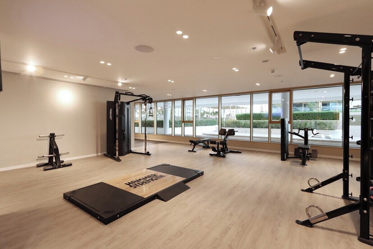 Et moderne fitnesscenter med forskellig træningsudstyr, store vinduer og trægulv.