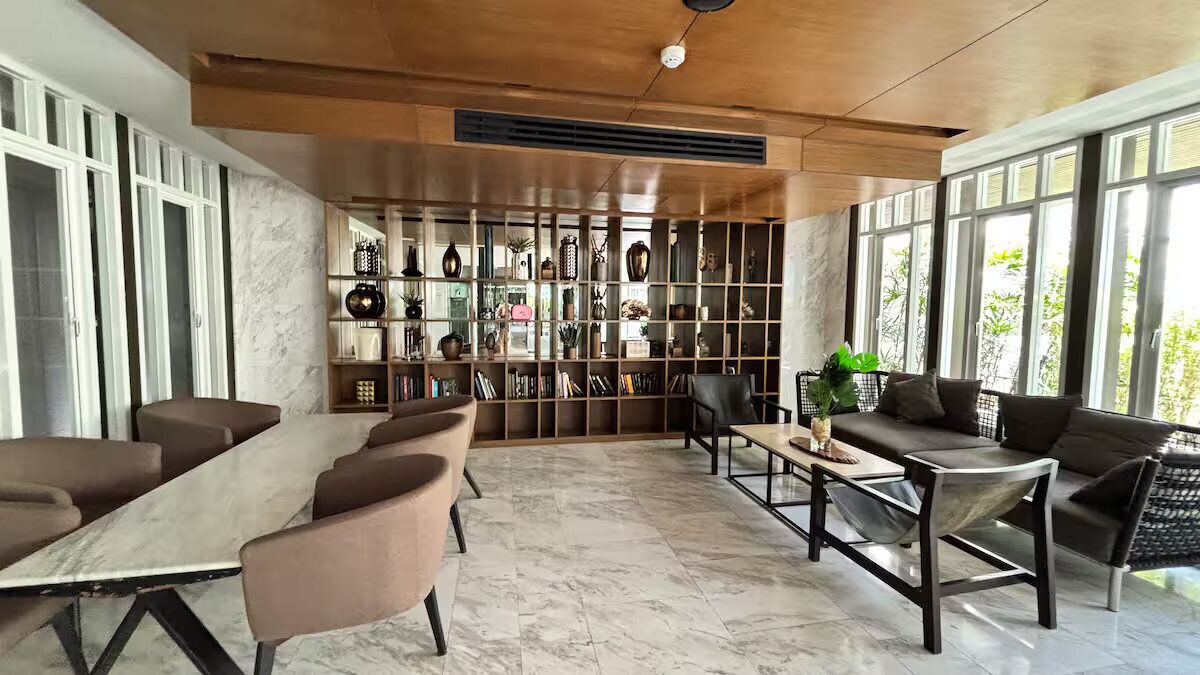 A modern interior with a long table and chairs, a sofa, and a bookshelf filled with decorative items.