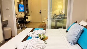 A hotel room with a bed, a desk, a chair, a television, and a dining area with a table and chairs. - The Base Downtown Phuket By Ploy (Wichit)