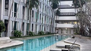 A modern building with a pool area, including lounge chairs and palm trees. - The Base Downtown Phuket By Ploy (Wichit)