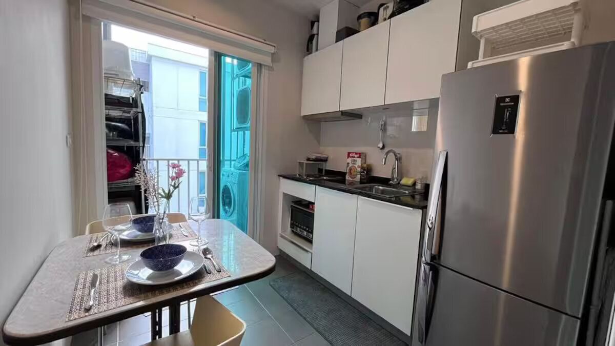 A compact kitchen with white cabinets, a stainless steel refrigerator, and a dining area with a table set for two.