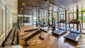 A gym with various exercise equipment, large windows, and a wooden floor. - The Base Downtown Phuket By Ploy (Wichit)