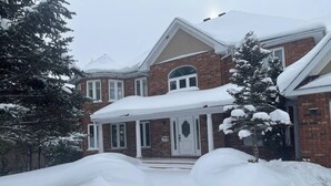 A large brick house with a covered porch and snow-covered trees.