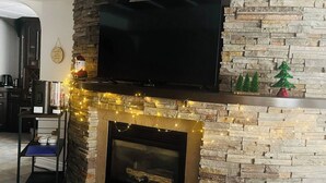 A living room with a stone fireplace, a flat-screen TV mounted above it, and a coffee table with a kettle and cups.