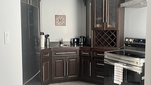 A modern kitchen with dark wood cabinets, a stainless steel refrigerator, a built-in oven, and a coffee maker.