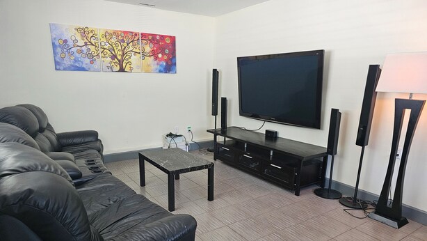A modern living room with a black leather sofa, a flat-screen TV, a coffee table, and a floor lamp. - Home sweet Home (Surrey)
