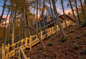 Een moderne cabin met een houten trap naar een terras, omgeven door bomen en herfstbladeren.