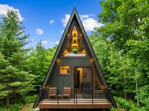 Une cabane triangulaire dotée d’un balcon, entourée de forêt.