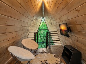 L’intérieur d’un chalet en bois, avec un escalier menant à un balcon, un téléviseur fixé au mur et un tapis en peau de vache.