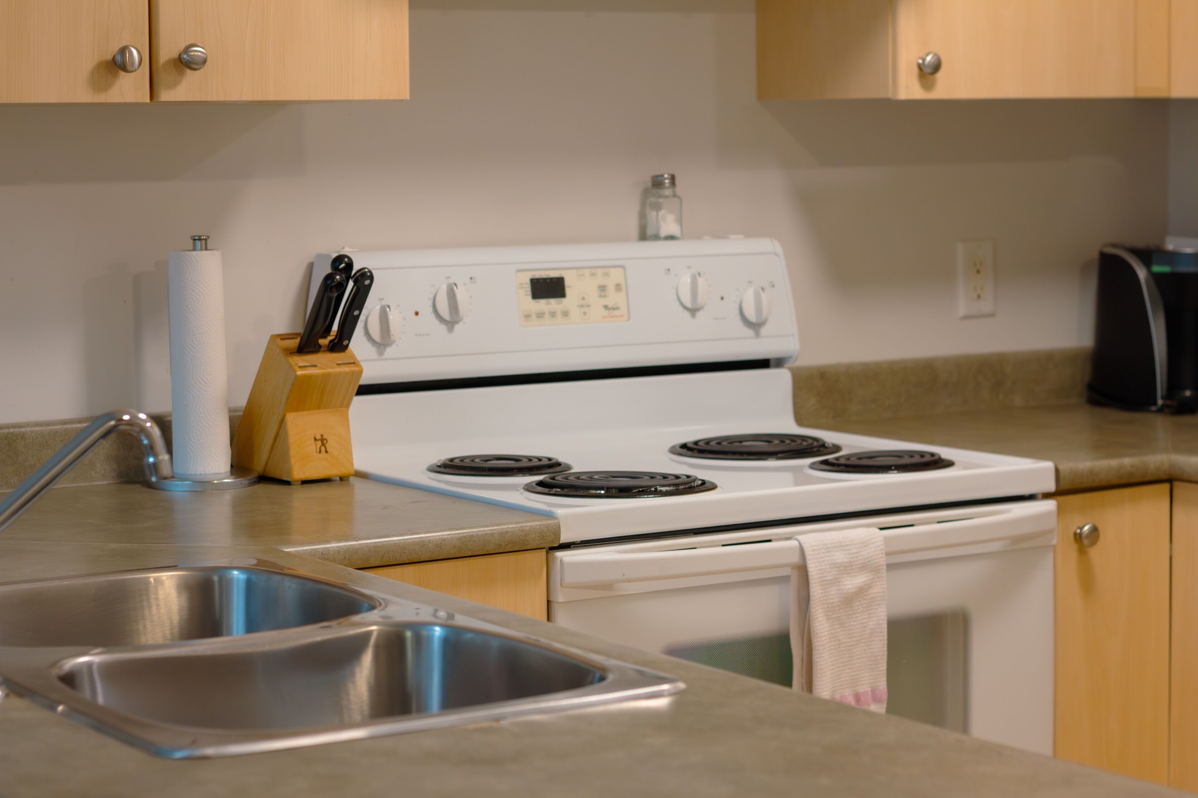 A kitchen with a white stove, stainless steel sink, wooden cabinets, and a coffee maker.