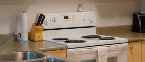 A kitchen with a white stove, stainless steel sink, wooden cabinets, and a coffee maker.