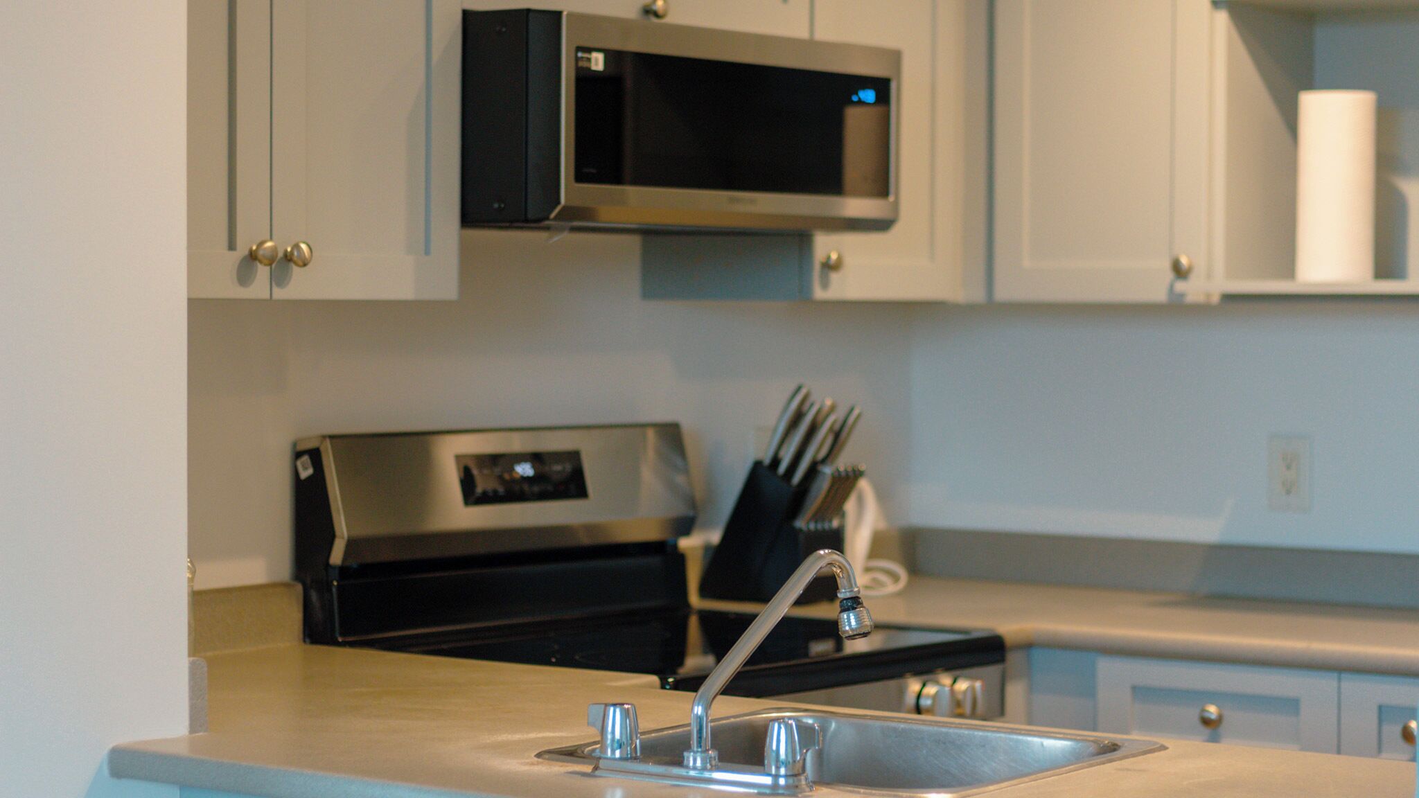 A kitchen with a stainless steel sink, a microwave above the stove, and a knife block on the counter.