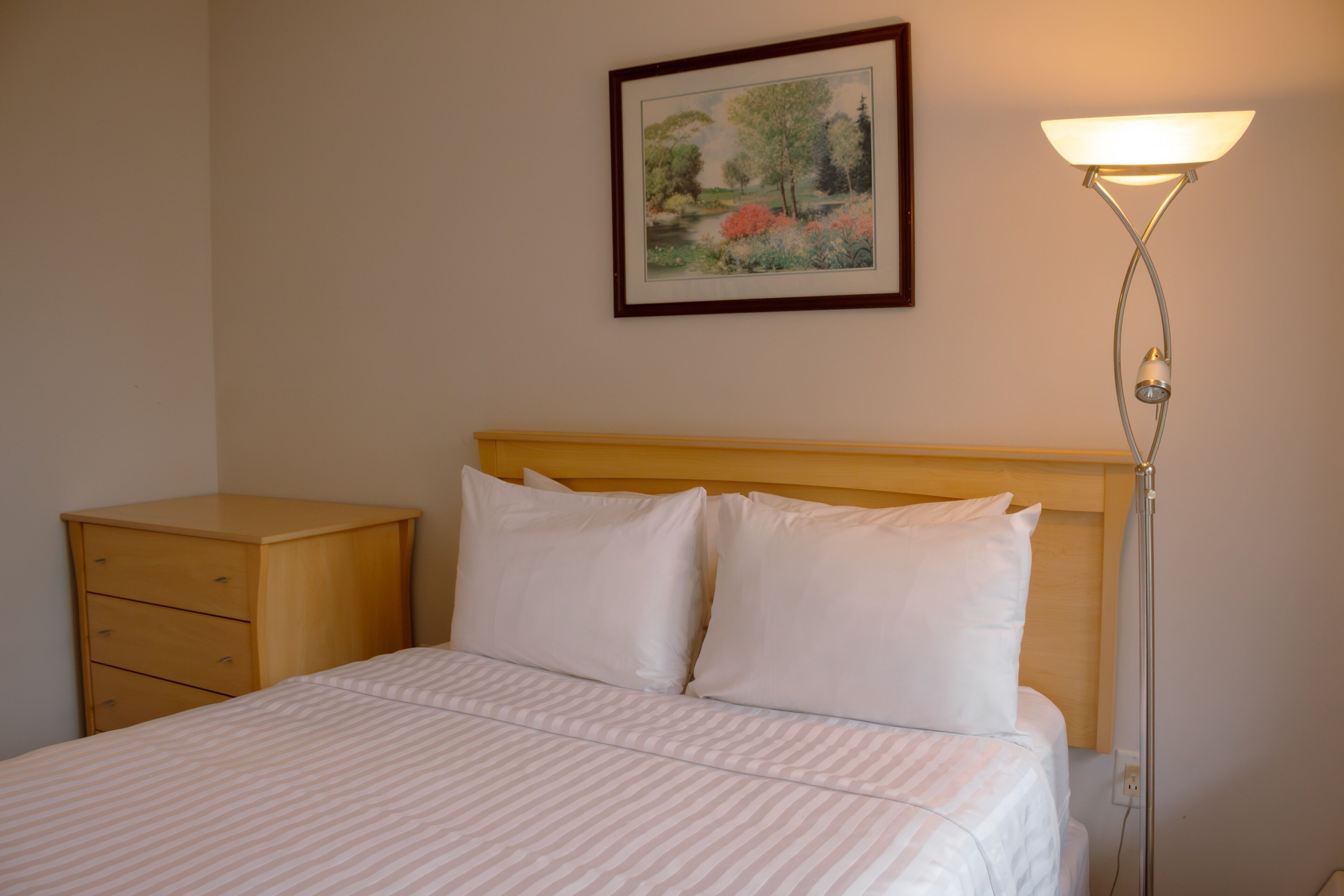 A neatly made bed with a headboard, a bedside table, and a wall-mounted lamp.