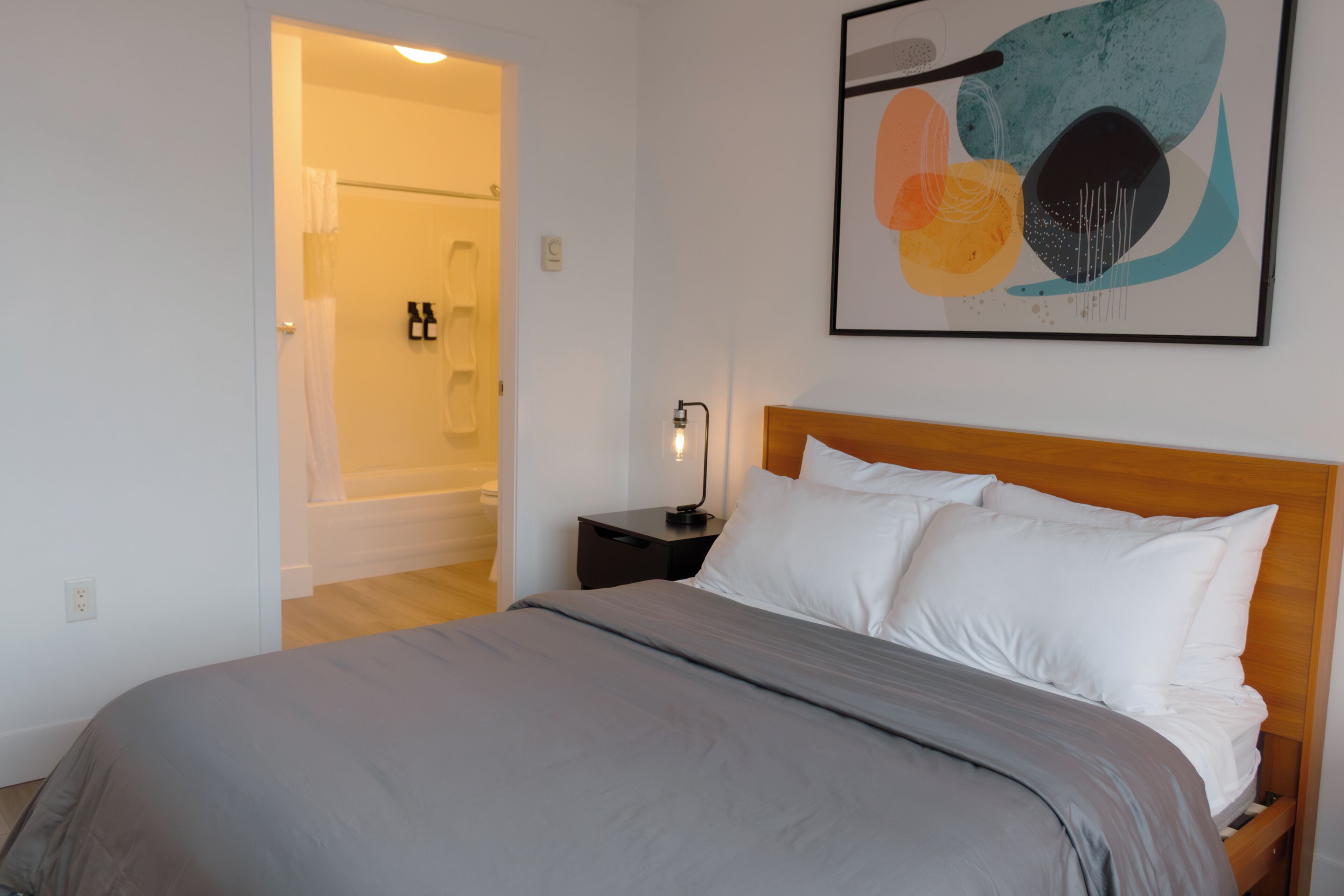 A bedroom with a bed, nightstand, and a painting on the wall.