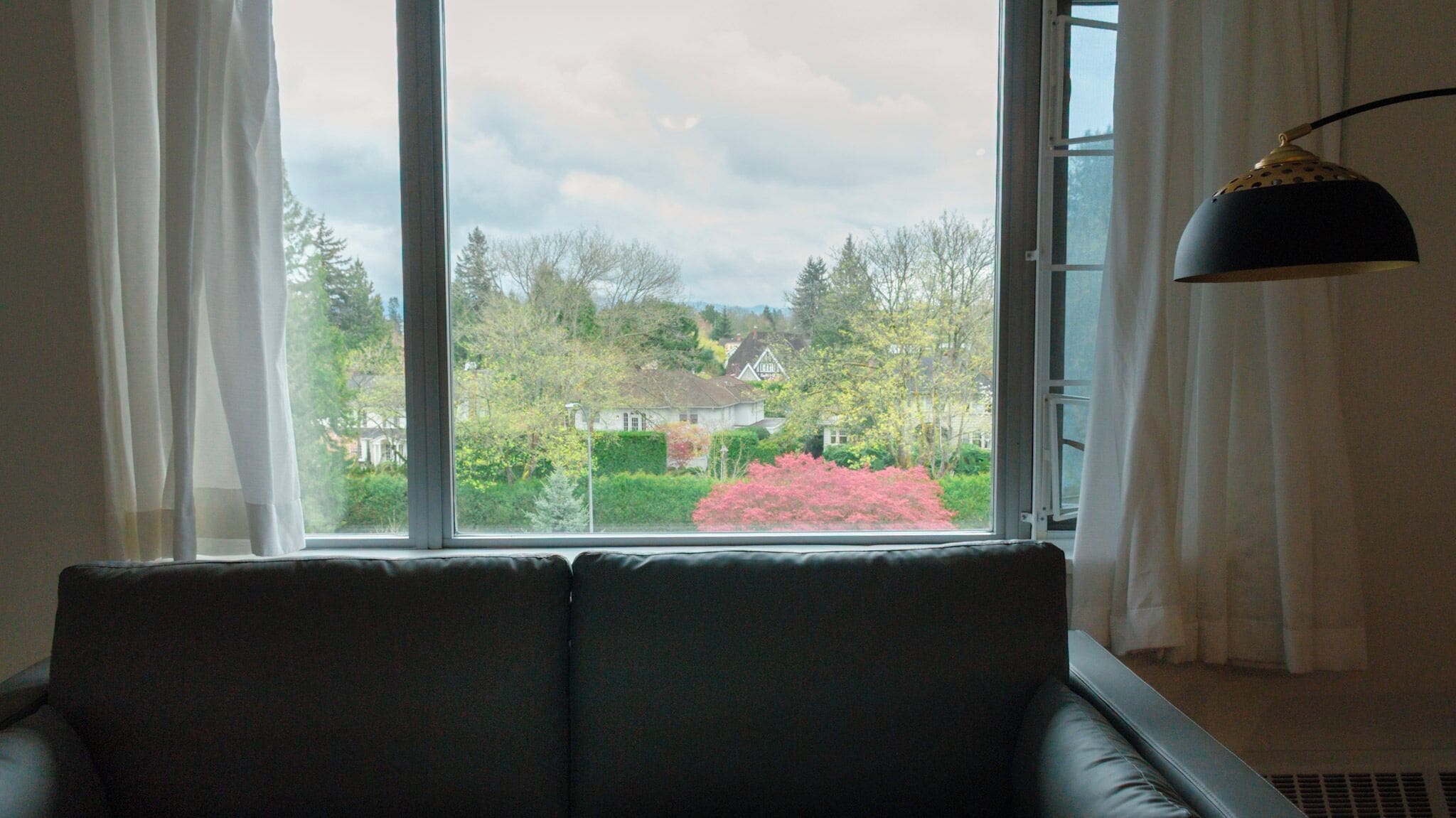 A living room with a large window, a black sofa, and a black floor lamp.