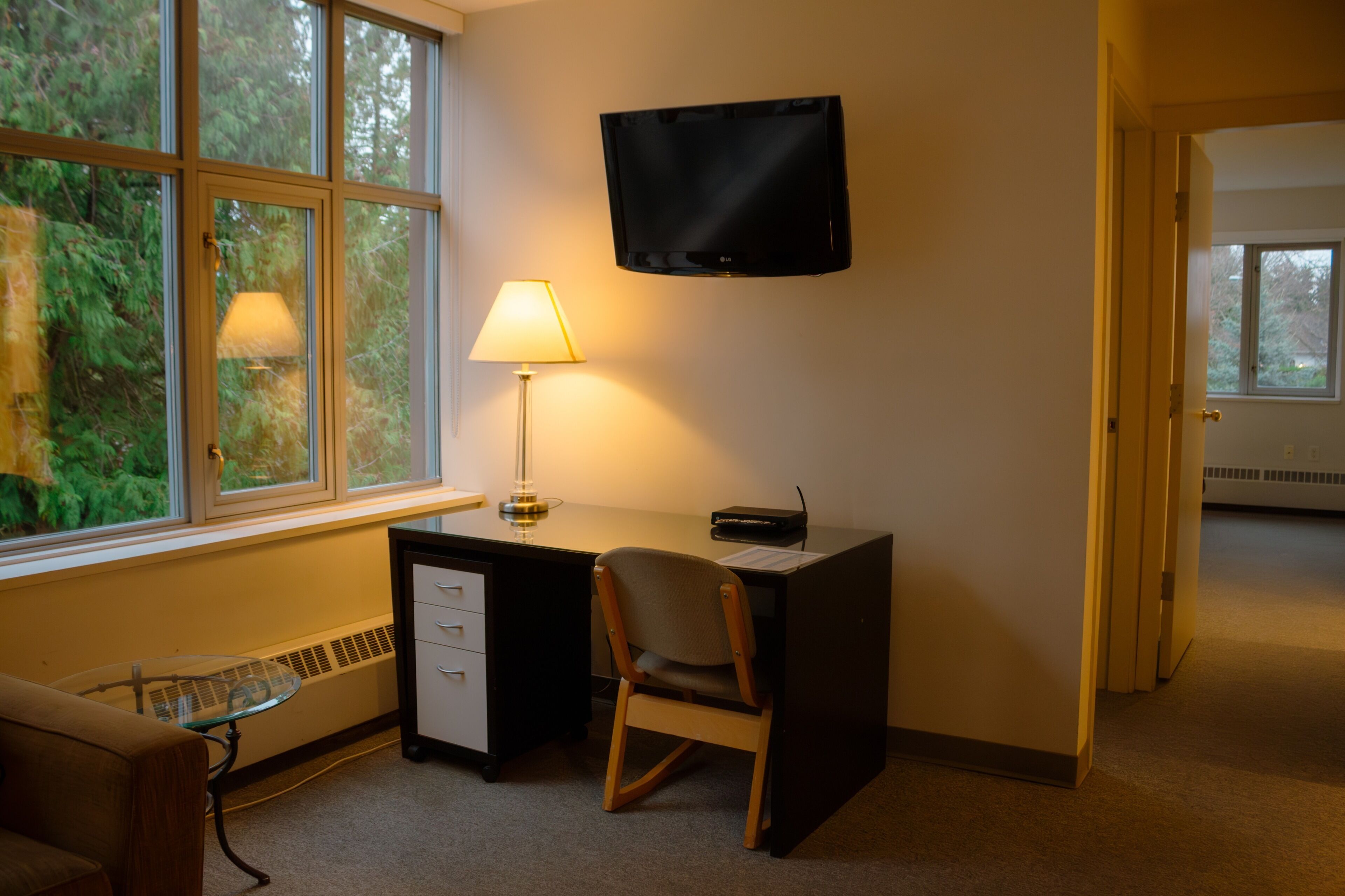 A room with a desk, chair, lamp, and a TV mounted on the wall.