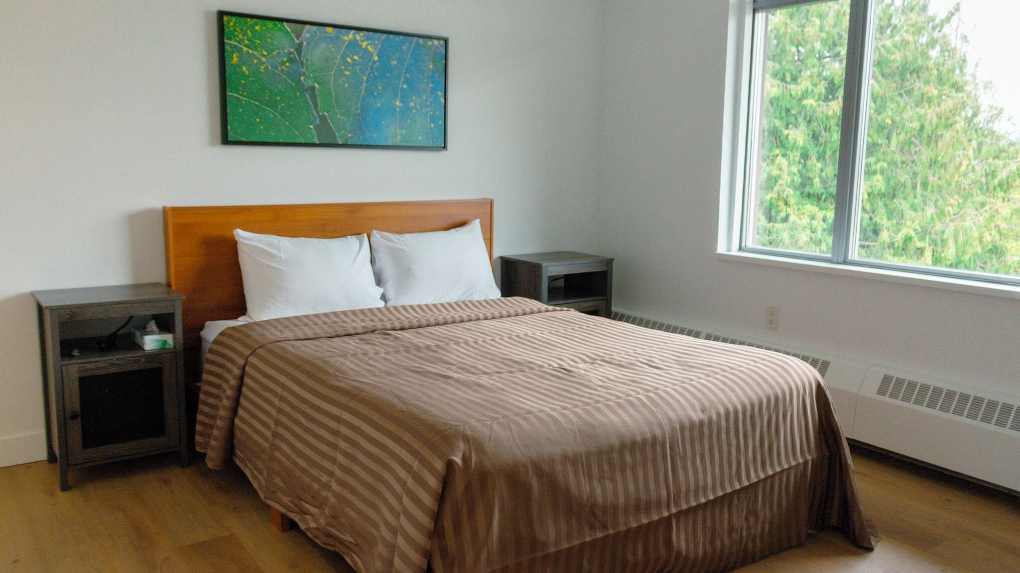 Ein Schlafzimmer mit einem Bett, zwei Nachttischen, einem Fenster mit Blick und einem Gemälde an der Wand.