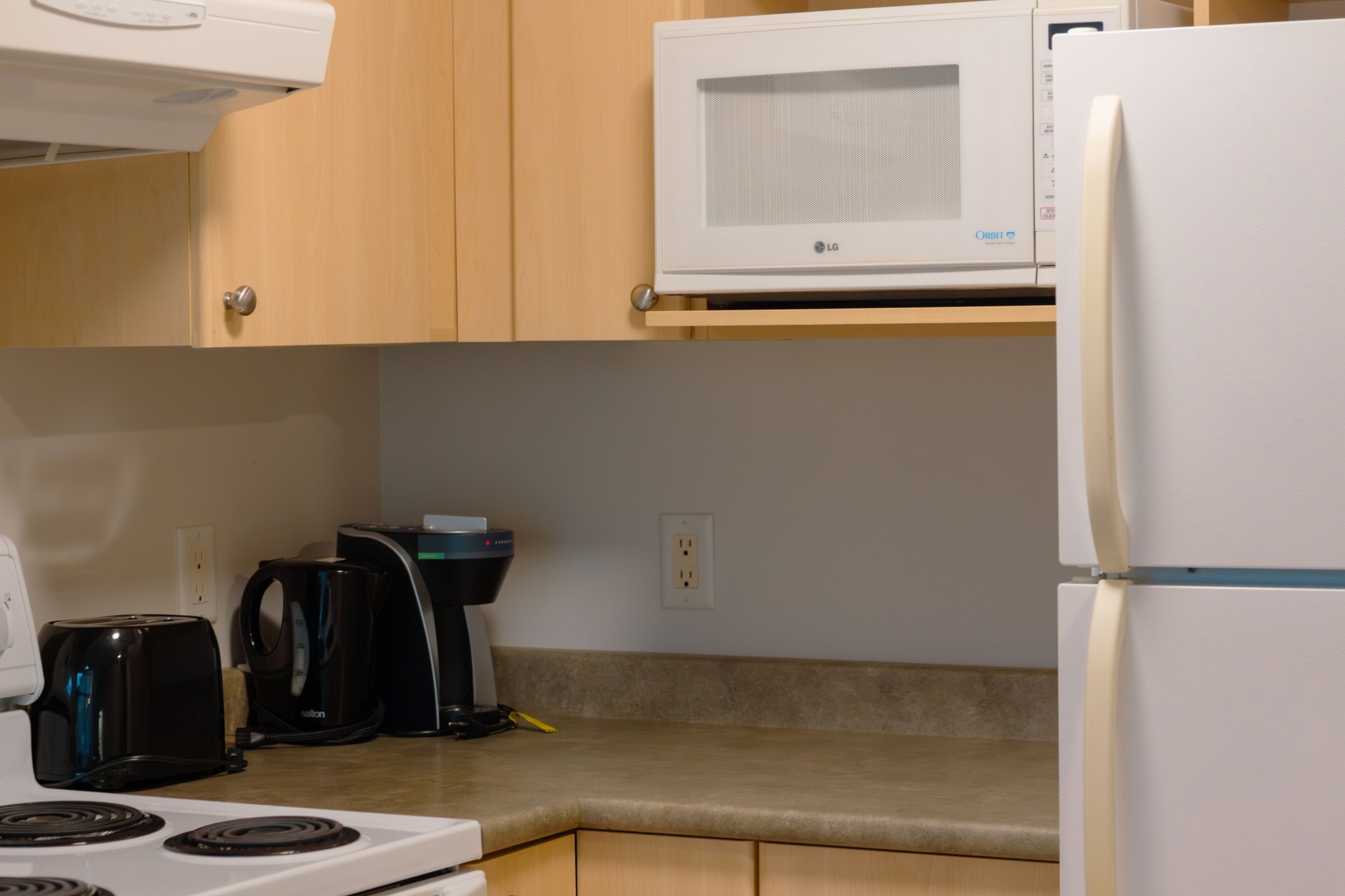 Una cocina equipada con microondas, tostadora, cafetera y refrigerador.