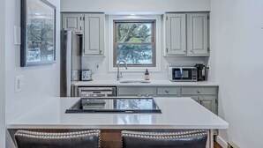A modern kitchen with white cabinetry, a built-in island with bar stools, a large window, and a stainless steel refrigerator. - Sunny Condo with Golf Views, Windsor Village (Hartford)